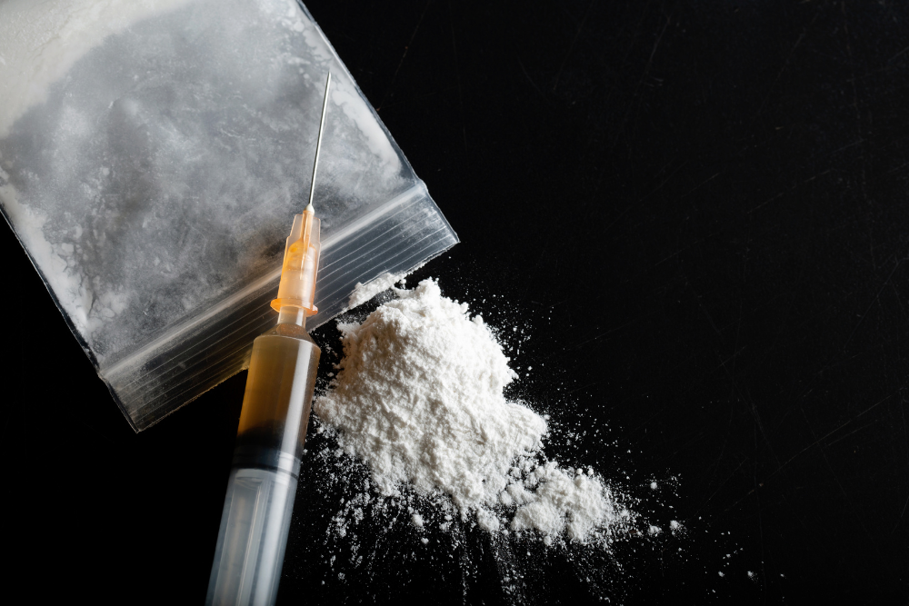 Spilled bag of heroin and filled drug syringe. Avenues Recovery discusses heroin addiction.