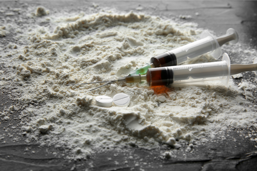 Cocaine powder on a table with syringes. Avenues Recovery details how to make cocaine hydrochloride powder