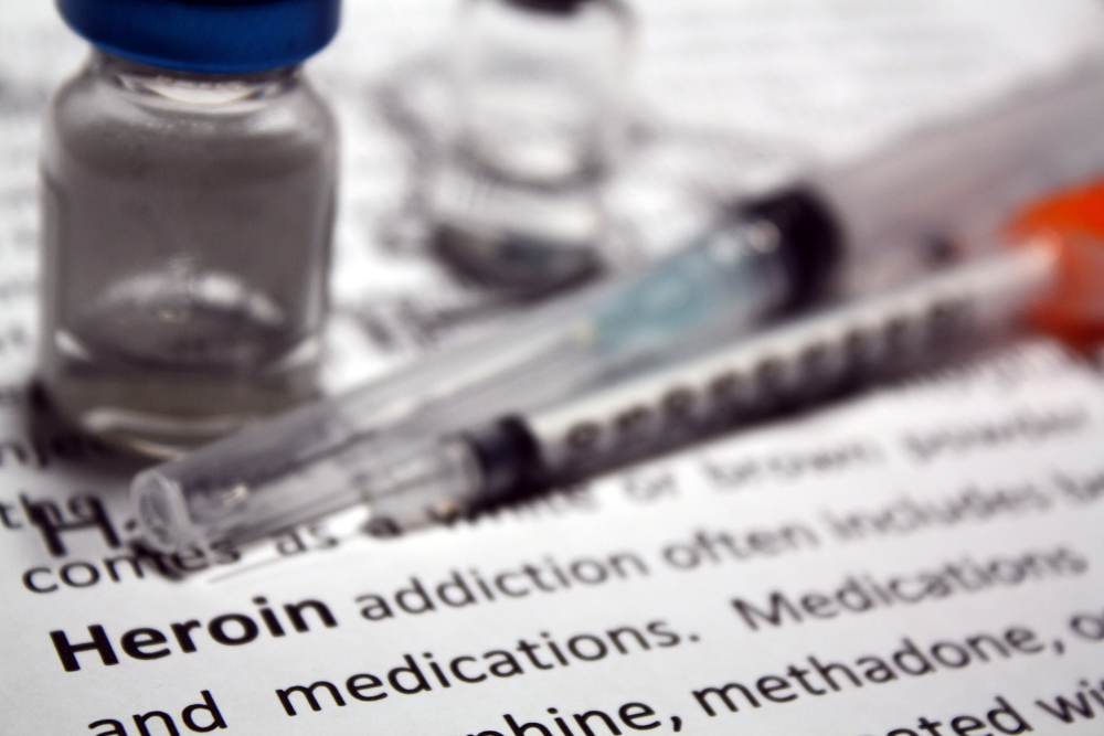 Drug syringes and bottle lying on text about heroin addiction, which is discussed by Avenues Recovery