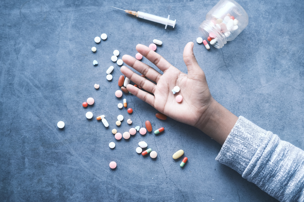 Outstretched hand of person who took overdose of MDMA or other drugs, surrounded by pills