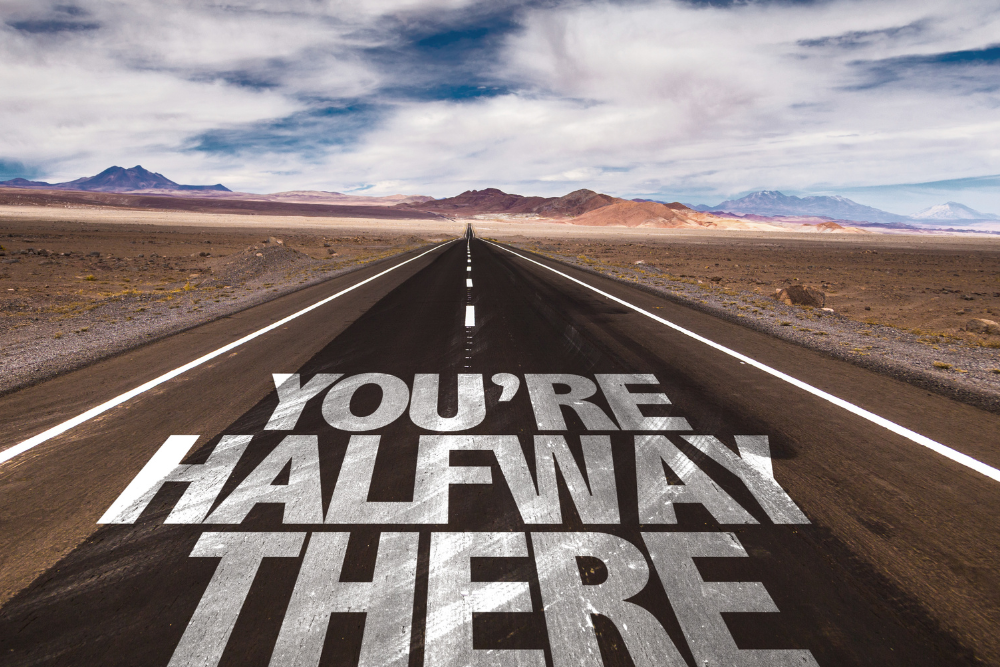 'You're halfway there' written on a desert road. Avenues Recovery describes what a halfway house is